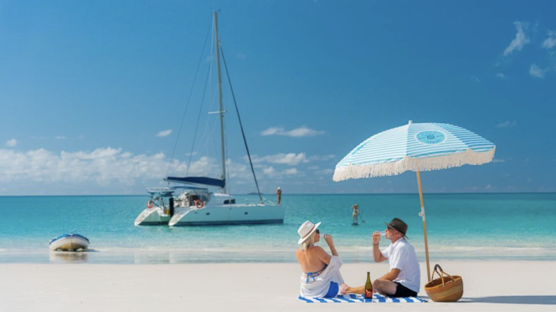 A couple having a picnic on Whitehaven Beach with a catamaran in the Whitsundays ocean