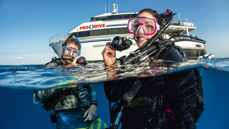 Two scuba divers happily surface after completing a 5-Day PADI Open Water Course with Pro Dive Cairns, enjoying their achievement.
