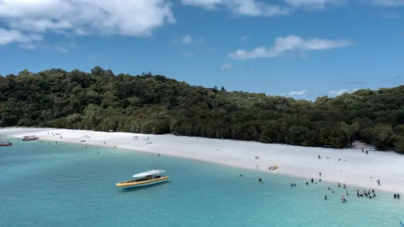 Stunning tropical beach with powdery white sand, vivid turquoise waters, boats by Hill Inlet Lookout, and vibrant coral reef snorkelling sites.