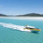Yellow speedboat glides by Whitehaven Beach, lush Whitsunday hills and top Coral Reef snorkelling sites visible in turquoise waters.