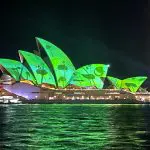 Sydney Opera House illuminated at night, viewed from a Sydney Harbour Vivid Lights cruise with canapés, reflecting vibrant green lights.