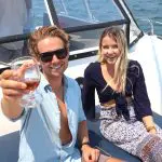 Two happy friends toast with wine on a catamaran, enjoying stunning Sydney Harbour views and sparkling blue water in the background.