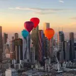 Vibrant hot air balloons soar above Melbourne skyline at golden sunset during a breathtaking 1-hour sunrise balloon flight experience.