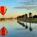 Soar in a red and white hot air balloon above a tranquil Melbourne lake at sunrise—book an unforgettable 1-hour balloon flight.