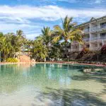 Luxurious outdoor pool surrounded by palm trees, loungers, and a modern hotel—ideal relaxation after your Kgari 2 Day Tour ex Hervey Bay.