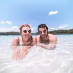 Happy couple wading in crystal-clear, shallow waters on a sunlit beach during Kgari Day Tour from Noosa, perfect for adventure.