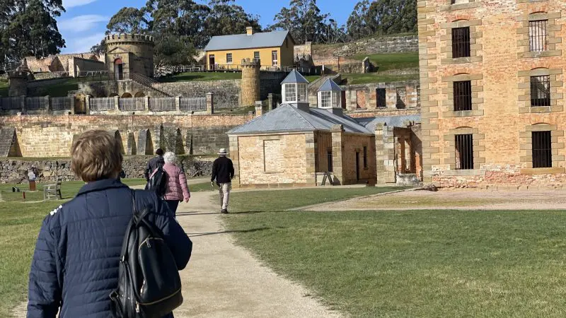Visitors stroll along a scenic path towards iconic stone buildings on a Tasman Safaris Port Arthur Harbour Cruise & Lunch Day Tour.