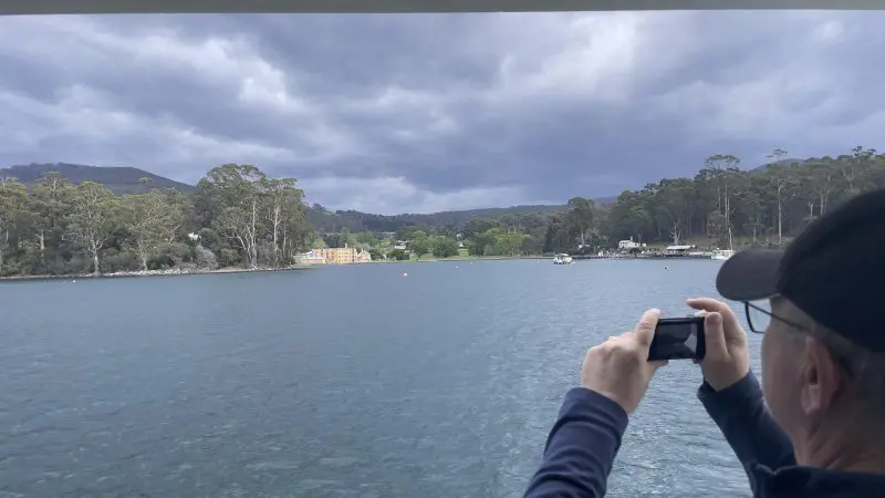 Traveller capturing stunning views of a pristine lake and lush forest on Tasman Safaris Port Arthur Harbour Cruise & Lunch Day Tour.