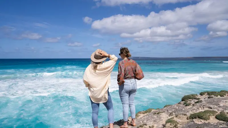 Two women admire the ocean from a rocky cliff during their 6 Day Eyre Peninsula and Flinders Ranges Adventure Tour in Australia.