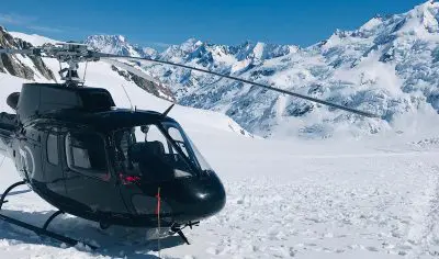 Sleek black helicopter on snowy Mt Cook mountain terrain, surrounded by stunning snow-capped peaks during a luxury alpine tour.