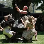 Group of friends cheer outdoors as a woman displays a wine bottle during a relaxed Yarra Valley winery tour, enjoying the scenic vineyard.