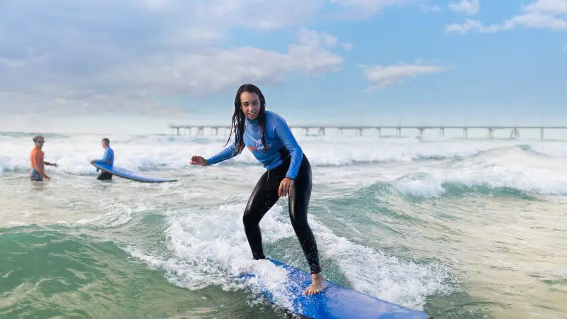 Woman in wetsuit skilfully rides a wave in a 2-hour beginner surf session for ages 13+, perfect for learning to surf confidently.
