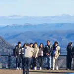 A smiling group enjoys panoramic Blue Mountains views at a scenic lookout on a guided waterfall walk and social lunch tour experience.