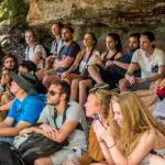 Tourists gather under a scenic Blue Mountains rock ledge on a 1 Day Wildlife Park Trip, engaging attentively with their expert guide.