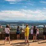 Travellers enjoy a panoramic Canberra Day Trip from Sydney, taking in stunning cityscapes, mountain vistas, and sparkling lakes under clear blue skies.