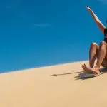 Smiling woman sandboards down golden dune with arms raised during a thrilling 1 Day Port Stephens Colourful Collective Travel tour.