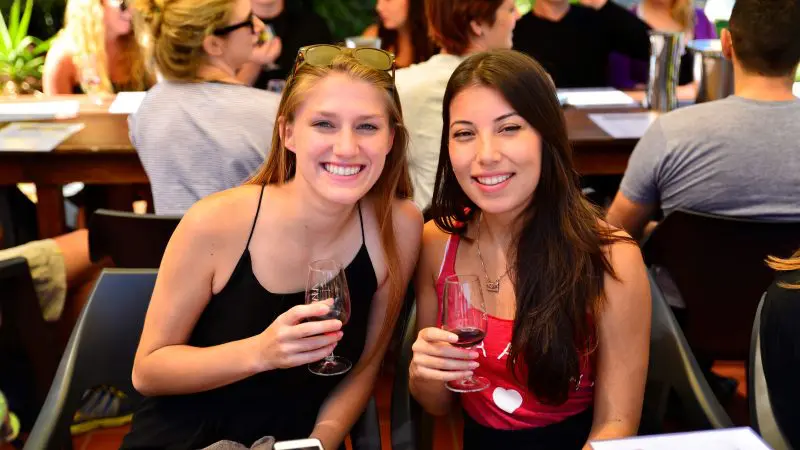 Two women savour red wine outdoors on a 1 Day Hunter Valley Wineries Tour from Sydney with Colourful Collective Travel, scenic vineyard views.