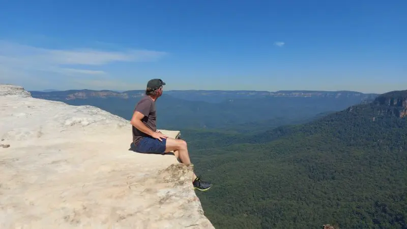 Traveller enjoys panoramic Blue Mountains vista from a rocky cliff edge on an All Inclusive Signature Day Tour, basking in nature.