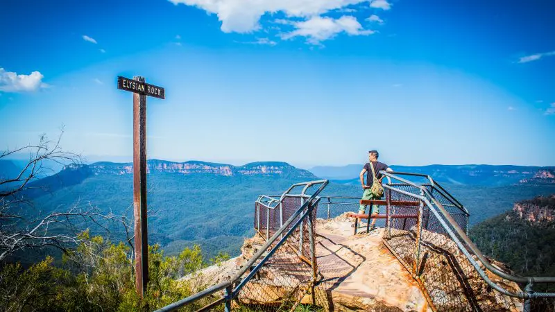 Traveller with Explorer Bus Pass stands atop Elysian Rock, poised to explore the breathtaking mountain vistas via hop-on hop-off tour.