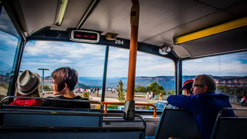 Passengers on the Boomerang Pass One Hour Sightseeing Tour coach enjoy panoramic mountain views through large windows beneath a cloudy sky.