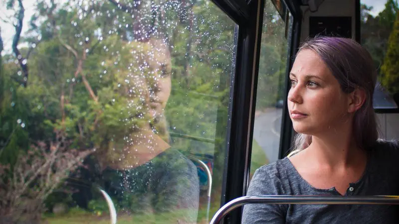 A woman with vibrant purple hair looks thoughtfully out a rain-spattered bus window on the Boomerang Pass One Hour Sightseeing Tour.