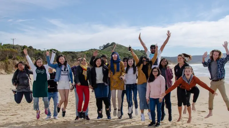 Happy travellers leaping on Bruny Island’s sandy beach during a Tassie Tours Tasmania day tour, enjoying the scenic coastline.