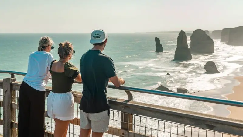 Three travellers on a wooden lookout admire stunning sea stacks, capturing the essence of Melbourne’s top coastal adventure experience.