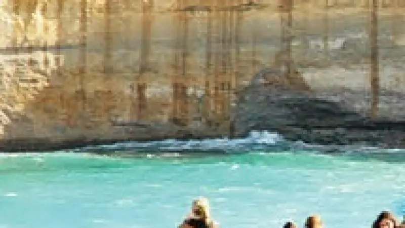 Tourists stand on a scenic wooden lookout platform overlooking dramatic coastal cliffs and crystal-clear turquoise waters on the Great Ocean Road.