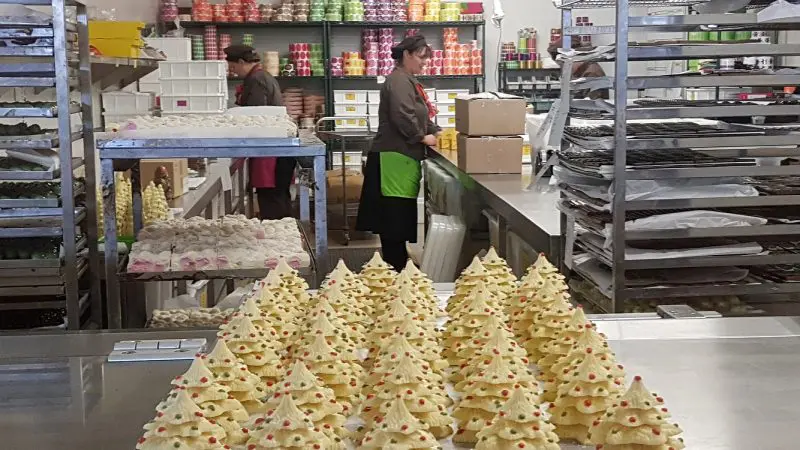 Rows of festive white chocolate Christmas trees showcased at Rayners Orchard Tour 1 in a vibrant, popular bakery kitchen setting.