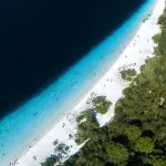 Stunning aerial view of Kgari 5 Day Ultimate Beach with pristine white sand, crystal-clear turquoise water, lush greenery, and visitors enjoying the sun.