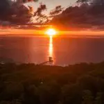 Stunning sunset illuminates the Kgari 5 Day Ultimate pier extending from lush forest to tranquil sea, perfect travel destination.