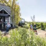 Visitors emerge from a charming rustic building near lush vineyards on a Coal River Valley Wine and Gin Safari, enjoying scenic views.