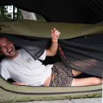 A smiling man in casual T-shirt and shorts relaxes inside his tent during a K’gari Swag Adventures Fraser Island tour experience.