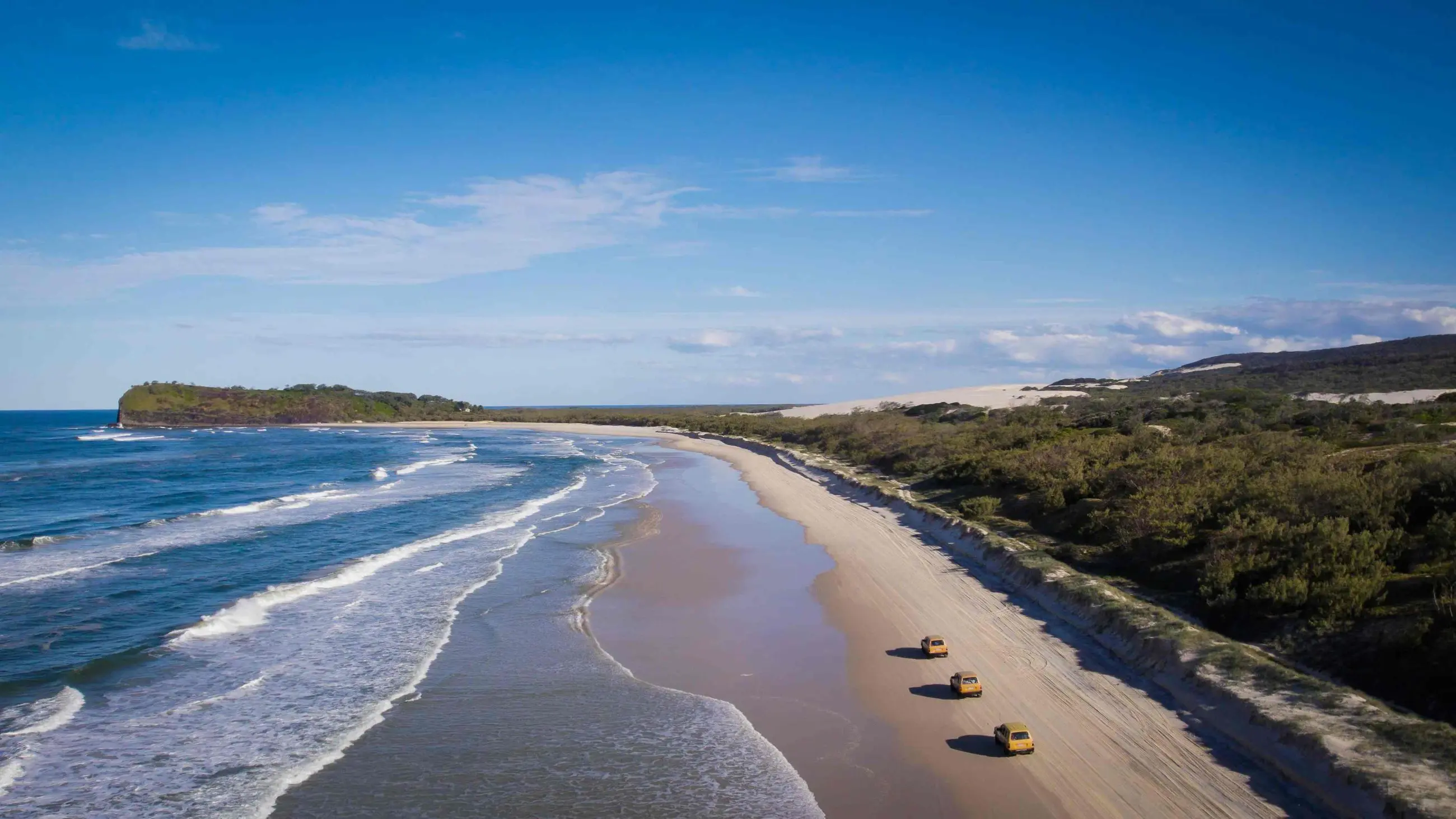 Drone shot of three bright yellow 4WDs driving along Fraser Island beach on K'gari Swag Adventures Tag Along Tour, Australia.