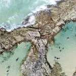 Aerial shot of tourists swimming in crystal-clear turquoise Fraser Island rock pools on a K'gari Safari 4WD tour from Noosa or Rainbow.