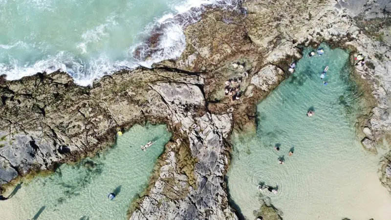Aerial shot of tourists swimming in crystal-clear turquoise Fraser Island rock pools on a K'gari Safari 4WD tour from Noosa or Rainbow.