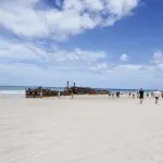 Tourists explore golden sands beside a historic rusted shipwreck on Fraser Island during the ultimate Kgari Safari 4WD camping experience.