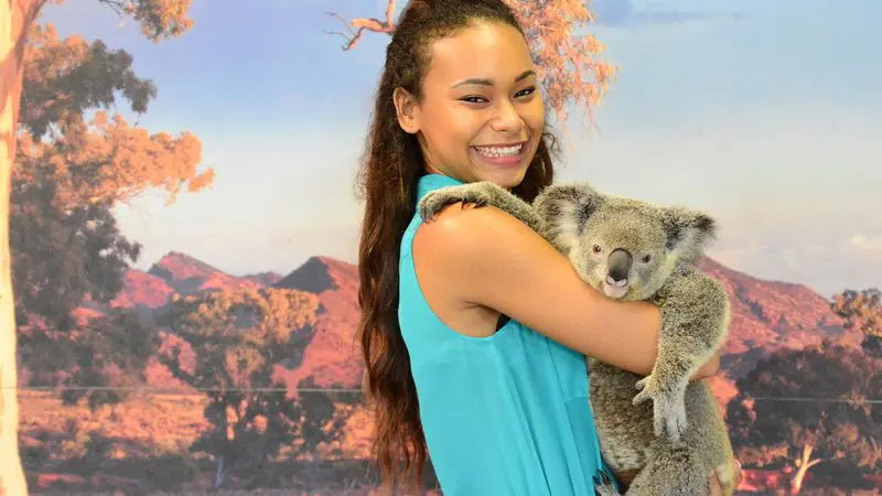 Happy woman in a blue dress holds a koala at Kuranda Koala Gardens, showcasing her 1 Day Kuranda Wildlife Experience Pass.