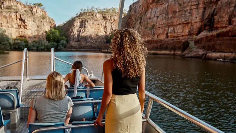 Three women on a 1 Day Katherine Gorge Cruise from Darwin, passing dramatic rocky cliffs and tranquil waters on a scenic adventure.