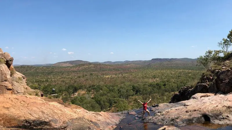 Adventurer atop rocky ledge during 4WD Kakadu tour, gazing over lush green valley and vibrant blue sky in Australia’s national park.