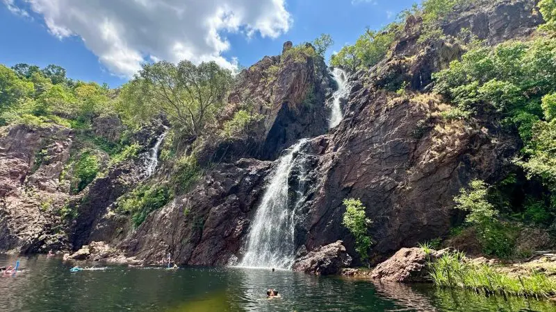 Stunning waterfall cascades over rocky cliffs near Kakadu Tour Hotel; twin stay for 2+, surrounded by lush greenery and clear blue sky.