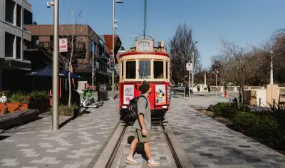 A man strolling along a city street beside a classic tram, urban scene, public transport, vibrant atmosphere, travel concept.