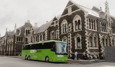 Vibrant green bus parked on roadside beside historic stone building, highlighting urban transport in scenic city environment.