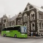 Vibrant green bus parked roadside beside a historic stone building, ideal urban transport near architecture, city street scene.