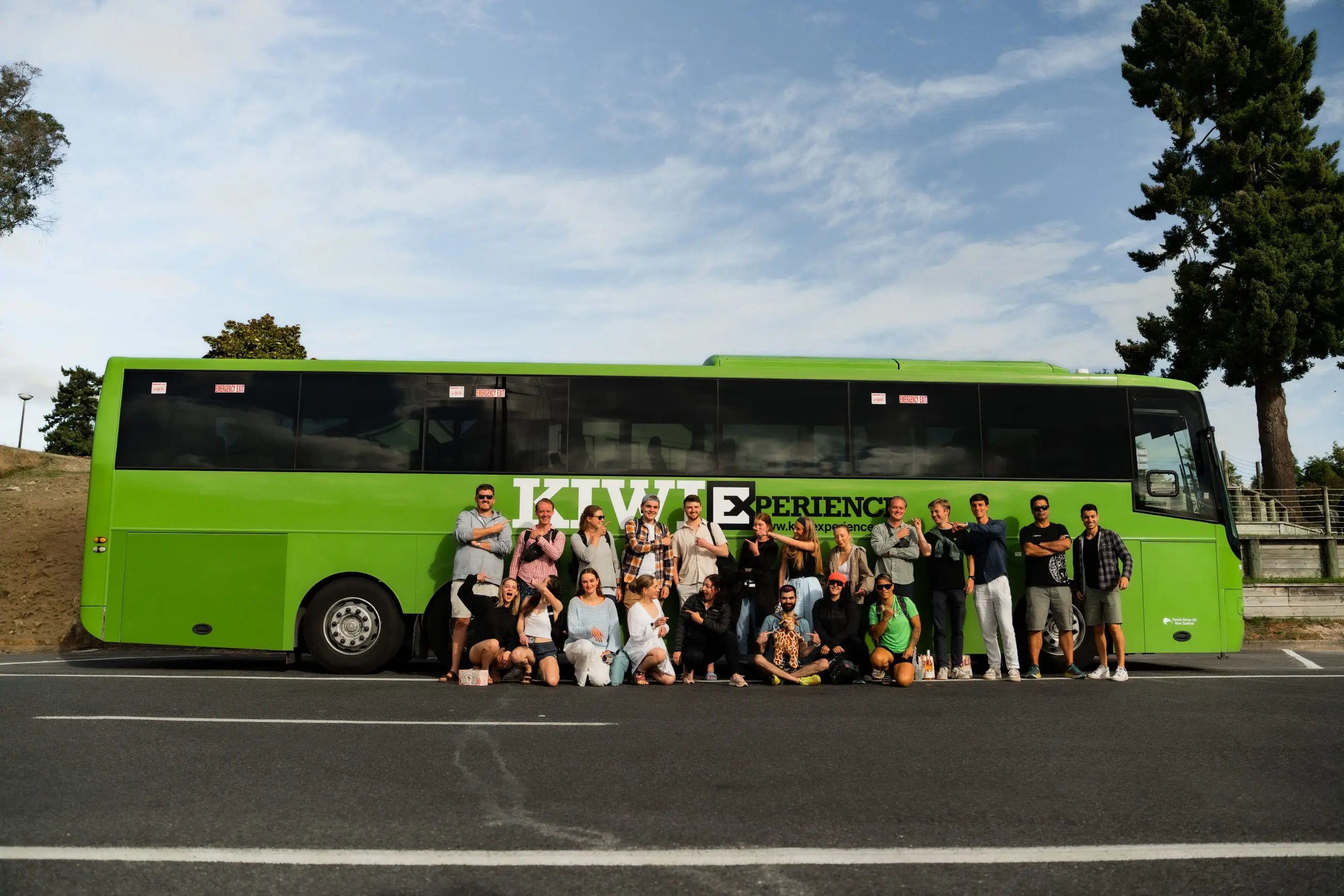 Diverse group posing in front of a vibrant green bus, performing the Funky Chicken pose for a fun, memorable photo opportunity.