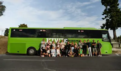 Diverse group posing in front of a vibrant green bus, performing the Funky Chicken pose for a fun, memorable photo opportunity.