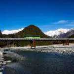 A fully loaded bus travels across a scenic bridge spanning a flowing river, showcasing transport over water in a picturesque setting.