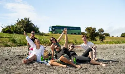 A diverse group of friends relaxes together on a sunny sandy beach, enjoying the sea view and warm weather under clear blue skies.