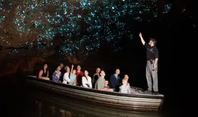 Adventurers in a boat navigate a dark cave, captivated by mesmerising glowing blue lights for a unique exploration experience.