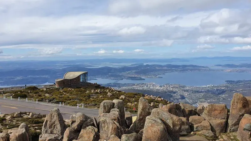 Breathtaking rocky mountain summit with a scenic hut, panoramic views of Lake Pedder on a guided wilderness day tour beneath cloudy skies.